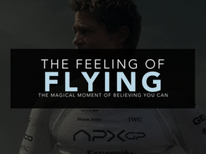White and pale blue text that reads "The feeling of flying. The magical moment of believing you can". This text sits on a black panel overlaying a darkly tinted photo of Brad Pitt from the movie F1. All rights of the film image remain the property of the owner.