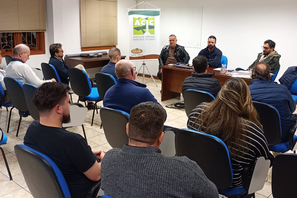 Reunião com várias pessoas sentadas em sala, diante de mesa com painel ACIC; clima sério e atento.