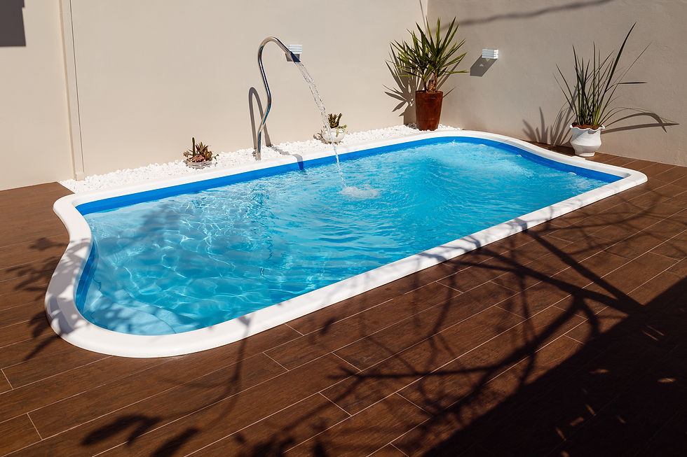Piscina azul com borda branca, cercada por plantas em vasos. Água flui de um tubo curvo. Piso de madeira ao redor sob luz do sol.