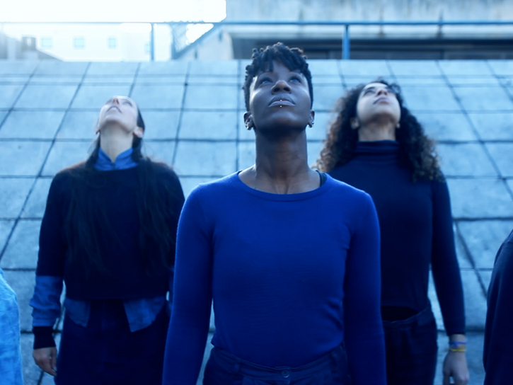 5 dancers dressed in blue stand looking at the sky.