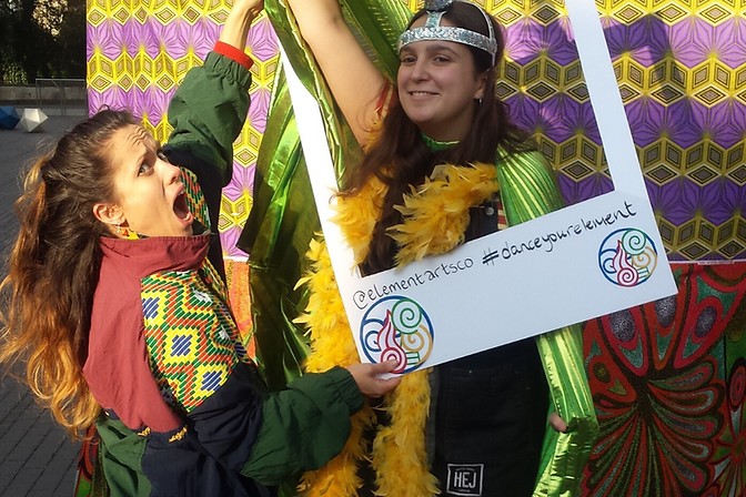 Showstoppers. -community dance event. A woman holds a large cut-out polaroid, with another woman in fancy dress coming through the frame