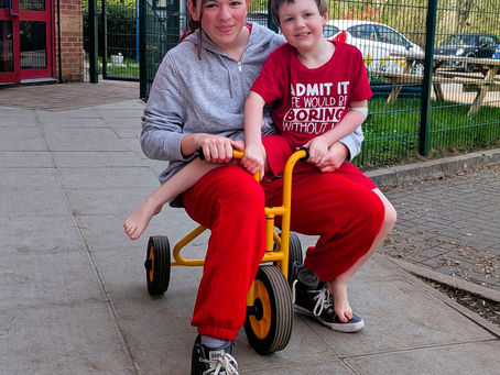 Two pupils sitting on a trike wearing red in support of Comic Relief