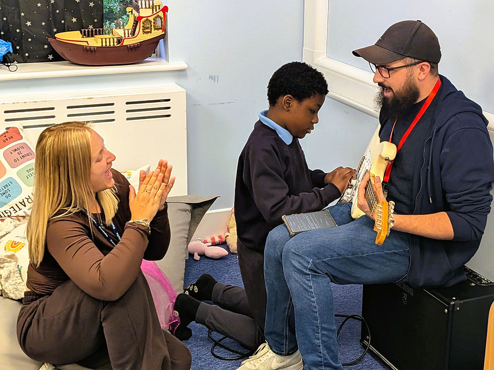 A Pupil from Bay Tree class playing guitar with Sam from Groove Studio, while a Teaching Assistant cheers and applauds