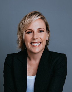 Kathryn is smiling, has blond shoulder length hair, wearing white jeans and top with a dar