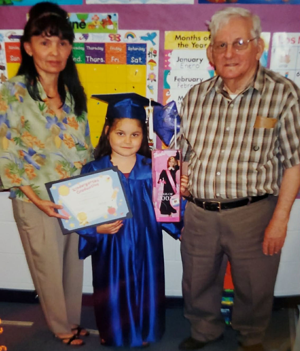 Owner Stephanie standing with her grandparents at her K5 graduation ceremony. Holding her certificate and a barbie doll her grandparents brought as a gift.