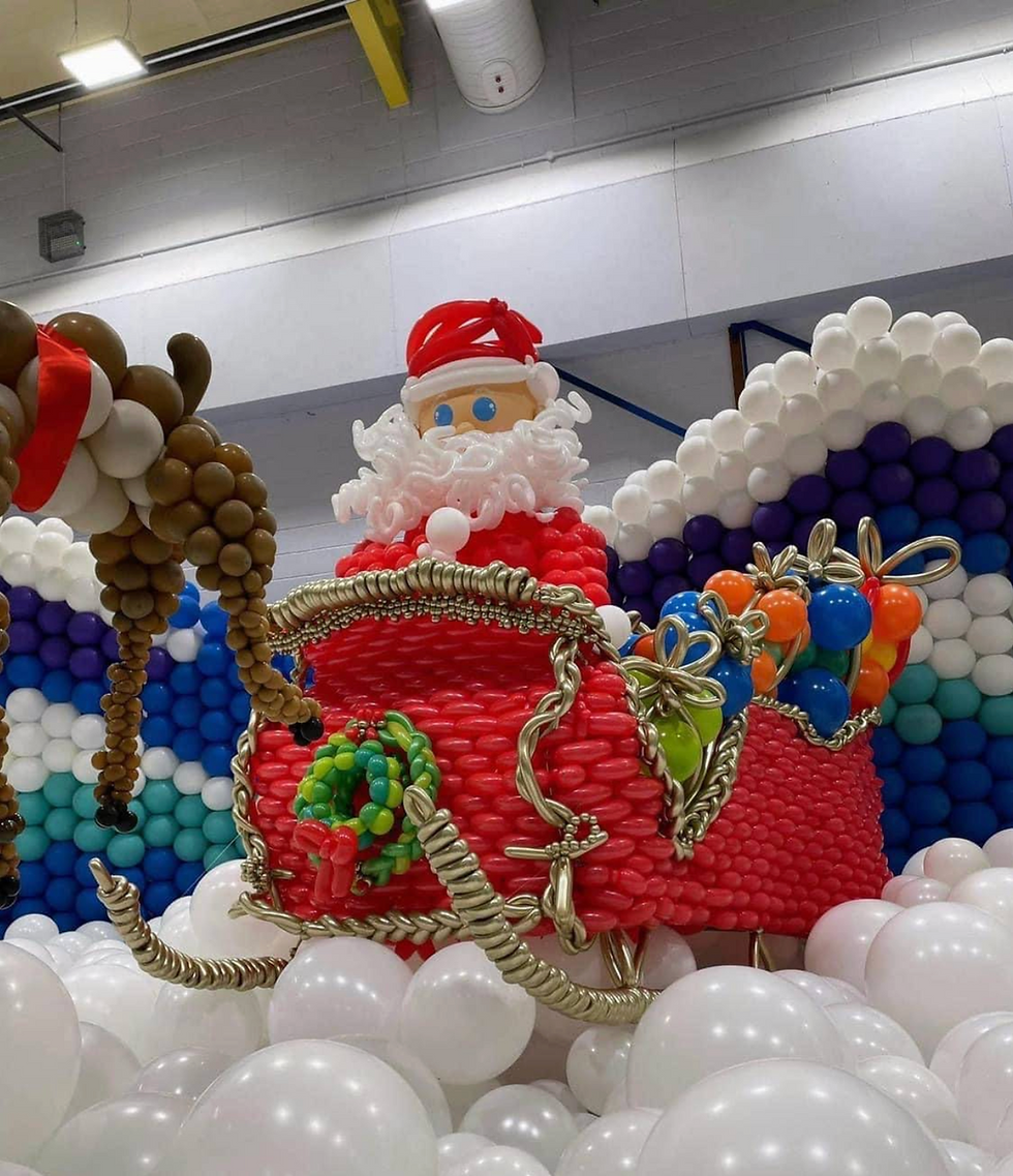 Oversized Christmas balloon sculpture featuring Santa in a red sleigh with presents and re