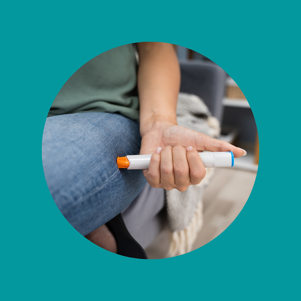 A woman injects an Epi-pen into the side of her thigh as she sits on a chair.