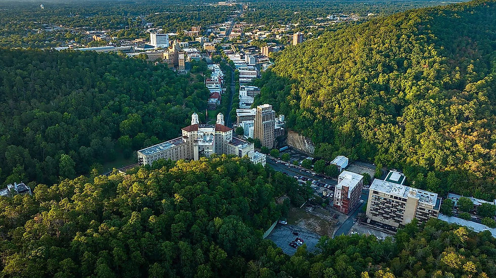 Aerial view of a city nestled between two lush green hills. Tall buildings and a busy street are visible. Clear sky and vibrant landscape.