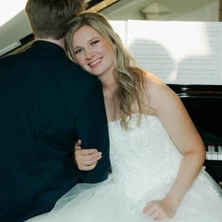 bride smiles at the camera as she leans on the groom. they both sit at the piano at at the broadway avenue, grand rapids michigan