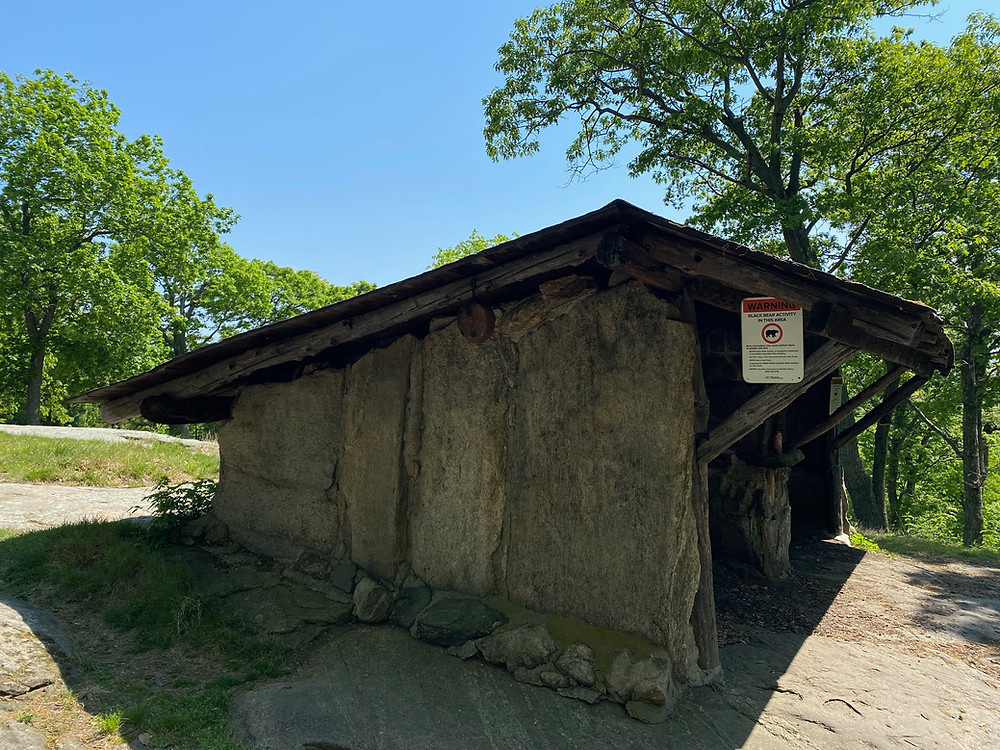 Stone built, roofed, hiking shelter on a sunny day. A bear warning hangs on the roof.