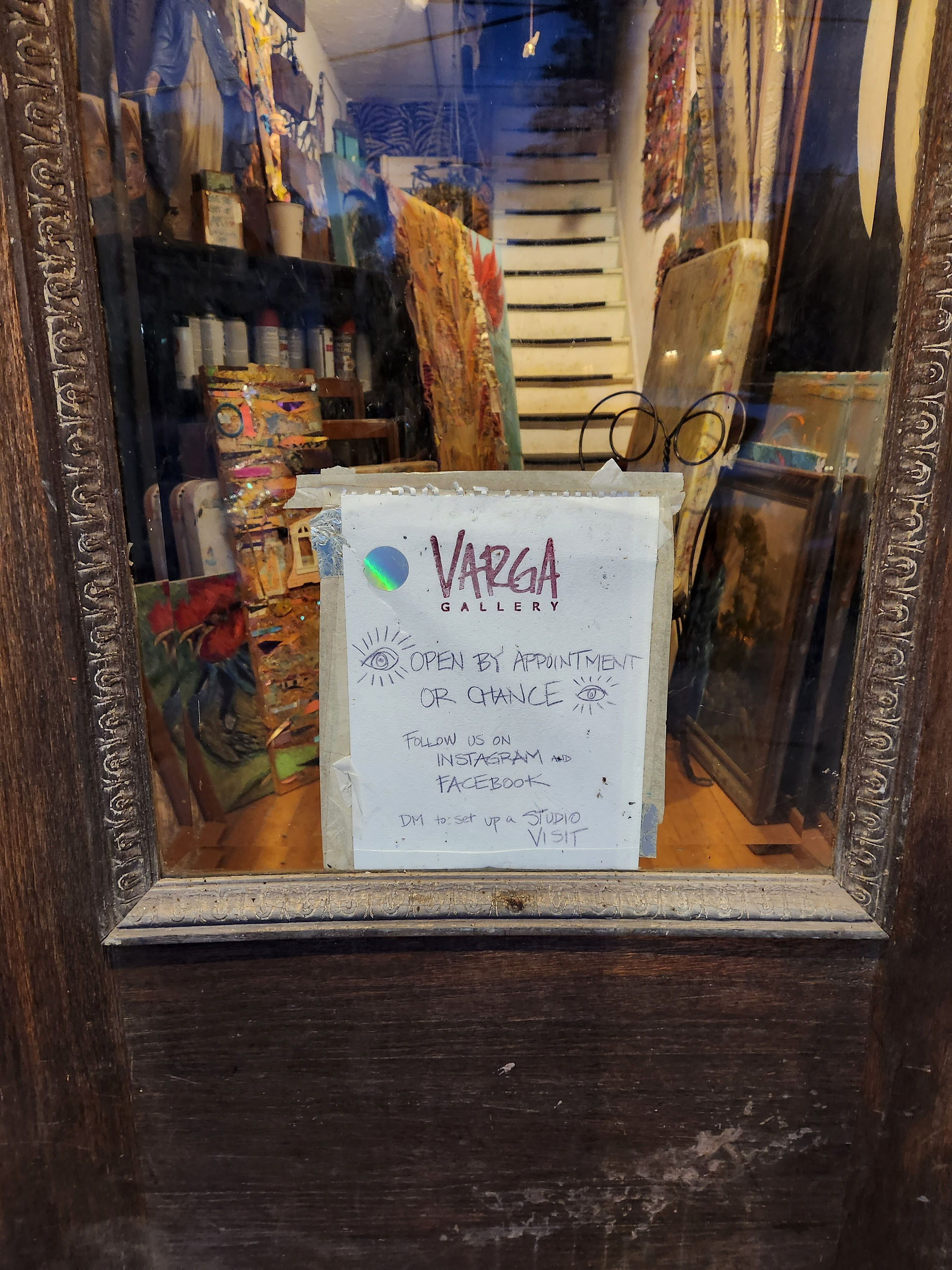 Hand decorated and written sign on the glass door of Phoenicia, New York art gallery with hours as, "Open by appointment or chance" with little eyes drawn next to the words.