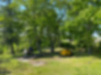 Two tents set up on a sunny day in a clearing between trees with a fire pit between them