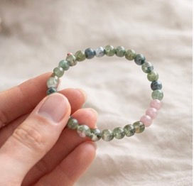 grey labradorite bracelet held between thumb & forefinger with a soft linen background