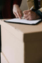 Hands signing a document on a clipboard placed on a cardboard box. One person points to the paper. Neutral colors, focus on action.