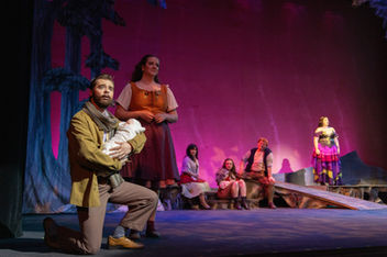 Man kneeling holding a baby with the mother behind and other actors behind her