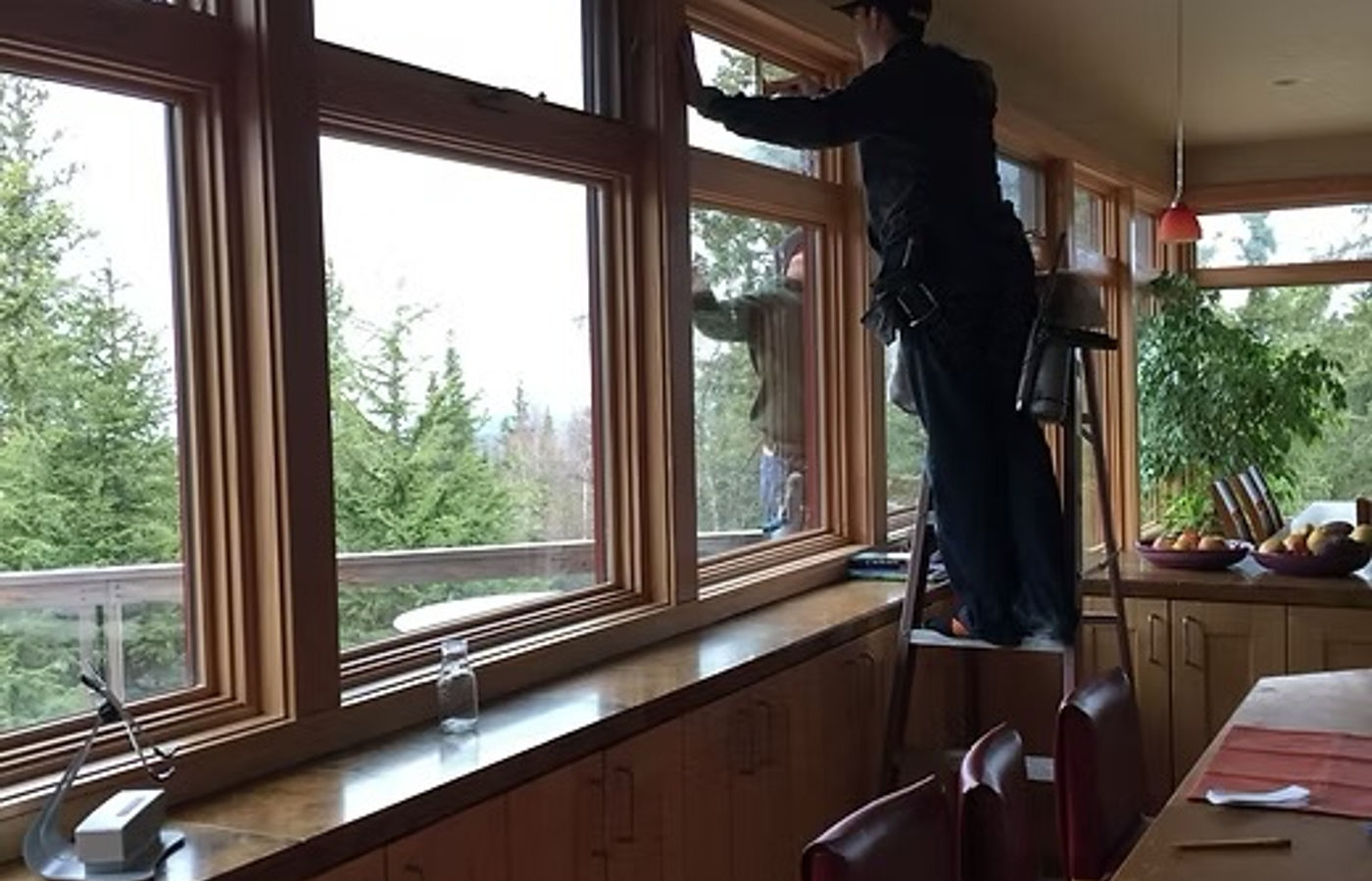 A.K. technician cleaning interior picture windows in an Alaska home overlooking the forest