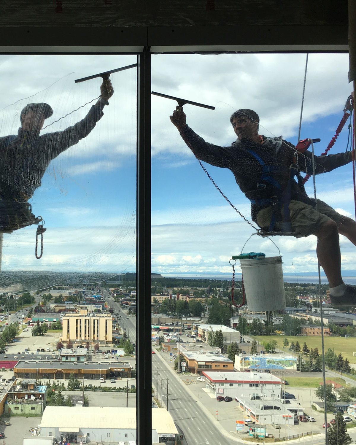 A.K. Window Cleaners technicians cleaning high-rise windows on rope descent above the Alaska skyline