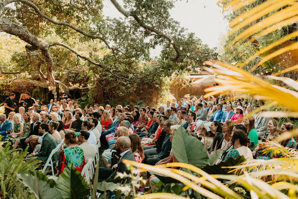 Large group of wedding guests gathered for a tropical ceremony surrounded by lush greenery and vibrant floral décor