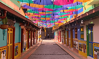 Colorful street in Guatapé, Colombia, with traditional buildings and bright umbrellas overhead.