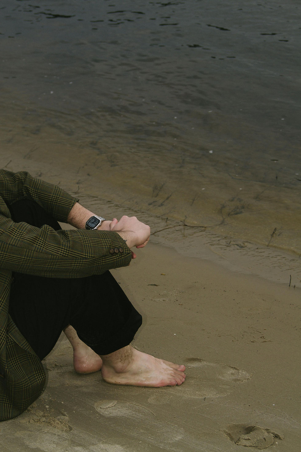 a man sitting holding his hands by the beach