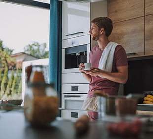 Man standing in a modern kitchen holding a coffee cup, looking out the window.