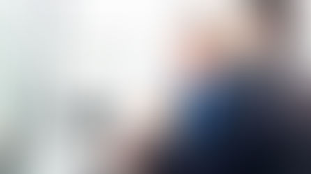 Two men in suits sit at a desk with multiple monitors, discussing work. The room is bright, creating a focused yet collaborative mood.