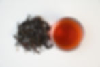 Ancient Tree Black Tea dry leaves with deep red infusion in a clear glass cup