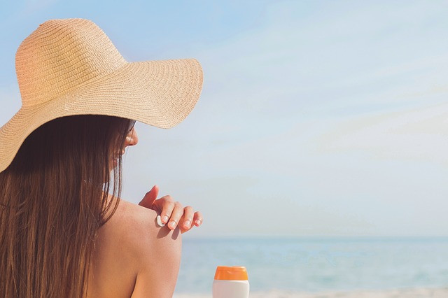 woman applying sunscreen and wearing a floppy hat