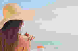 woman applying sunscreen and wearing a floppy hat