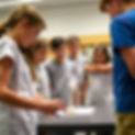 students in short sleeve shirts standing in a half circle looking down at an erupting cup