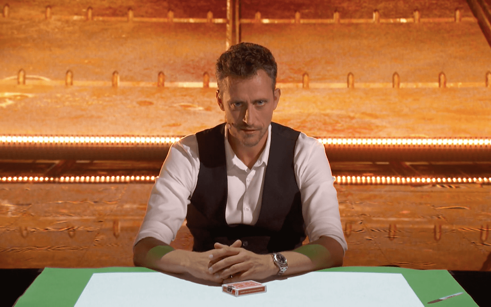 Un magicien présente discrètement un jeu de cartes, invités curieux dans un salon cosy.