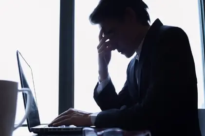 Man in dark suit sitting in front of a Laptop looking confused and upset