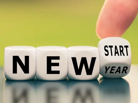 Finger rolls a cube from "NEW YEAR" to "NEW START" on a reflective surface. Bright green background suggests optimism and change.