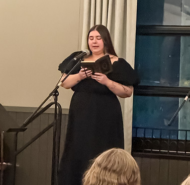 Woman in a black dress reading poetry during an event.