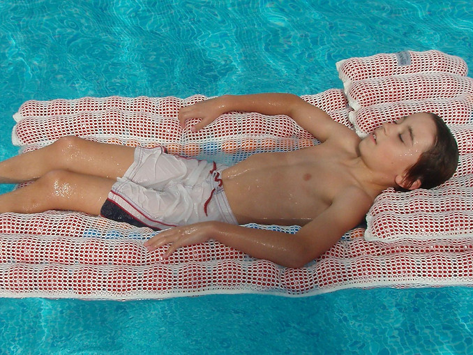 A young boy lying down on a Sensafloat device in a pool