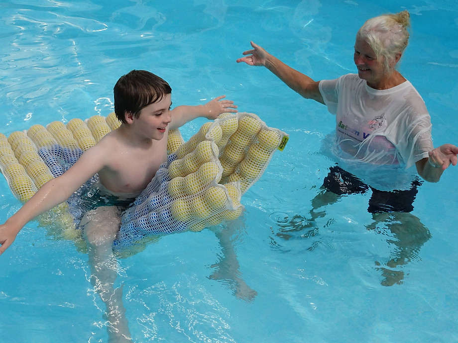 A student and an instructor in a pool. The student is sitting on a Sensafloat device