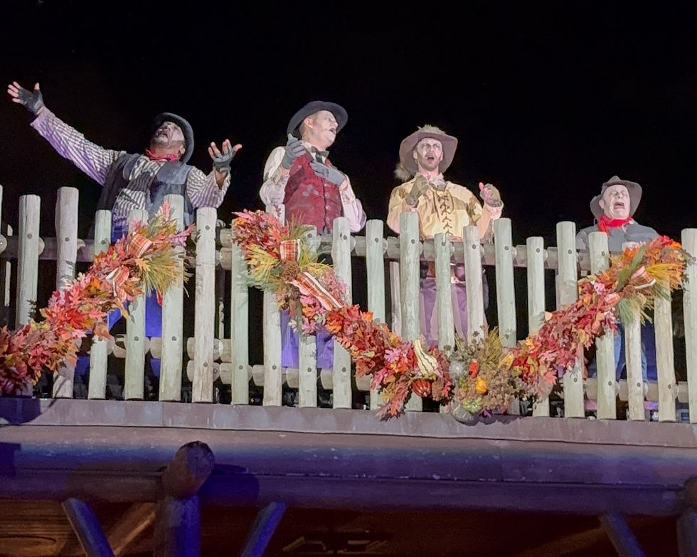 Four people in western attire sing joyfully on a wooden balcony decorated with autumn garlands, set against a dark night sky.