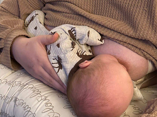 A baby nursing in cross cradle position on a boppy pillow with mother's hand supporting the back