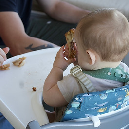 Baby practicing self-feeding during a baby-led weaning session in a high chair.