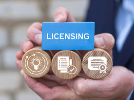 Close-up of hands holding wooden blocks with icons and a blue sign labeled “Licensing,” representing professional contractor licensing.