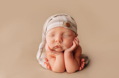 Baby in froggy pose on a tan blanket sleeping peacefully at photography studio.