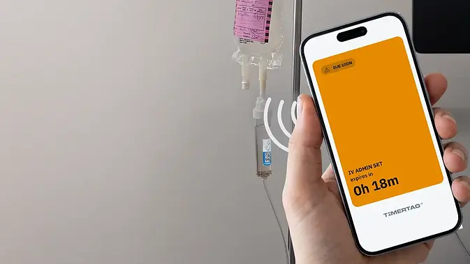 Timertag Pro label affixed to the drip chamber of an IV administration set with a user holding a smartphone near the label. A user experience screen is displayed showing a yellow screen with the remaining dwell time for the IV administration set. The dwell time is displayed within a yellow screen because the remaining dwell time is less than 2 hours.