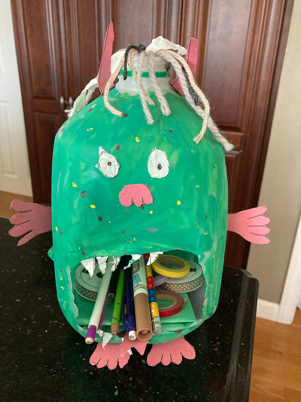 Plastic milk jug painted green with large eyes and mouth cut out to hold school supplies.