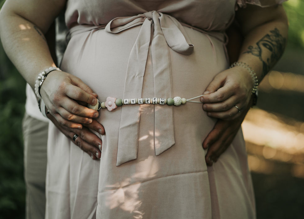 a pregnant woman wears a pacifier clip with the name ayleen on it