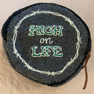 circular grey felt zipper pouch with barbed wire and "High on Life" embroidered on it in green.