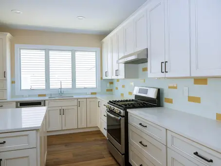 Newly installed white kitchen cabinets and countertops with a minimalist tile backsplash accented by yellow horizontal inserts.