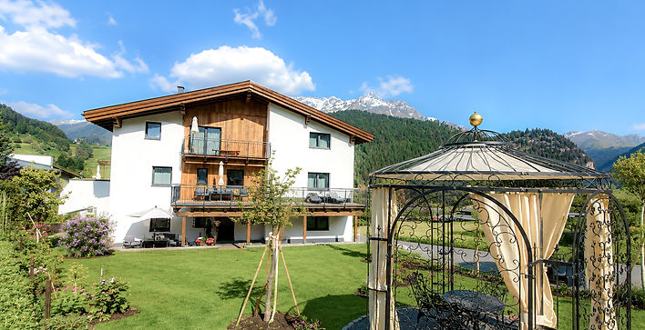 Ansicht Haus Alpenblick Fruehling mit Garten und Pavillon