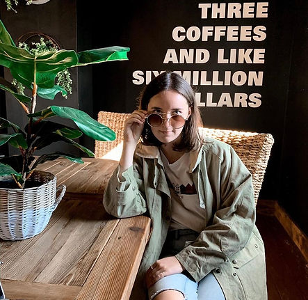 employee sarah sitting at table looking at camera half way lowering glasses wearing a green jacket
