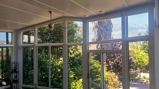 Large angled trapezoid windows framing a clear view of garden trees without shades in a sunroom in Denver CO — Blind Corners and Curves.; Experience superior skylight window treatments when you choose Blind Corners & Curves in Denver, Durango, and Steamboat Springs.; 