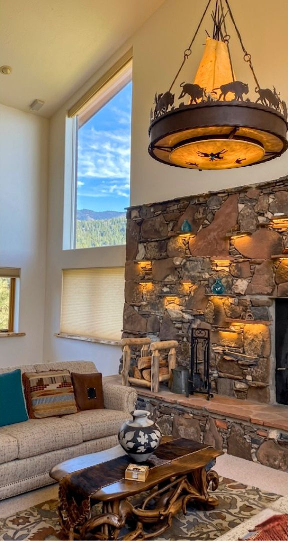 High architectural trapezoid windows left uncovered next to a large rustic stone fireplace to show mountain peaks and a clear blue sky — BCC of Denver Colorado.; Blind Corners & Curves provides low-maintenance specialty treatments for homeowners in Aurora, Aspen, and Durango.;